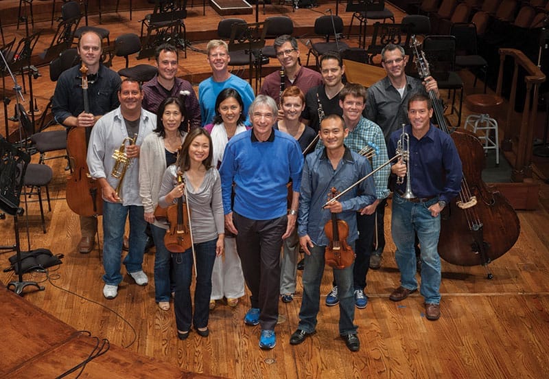 Michael Tilson Thomas stands smiling surrounded with with young musicians who are holding their instruments..
