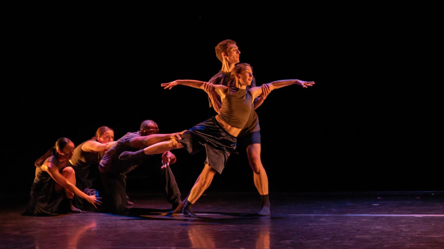 A group of dancers on stage. A man holds a woman in his arms as the other dancers pull at her.
