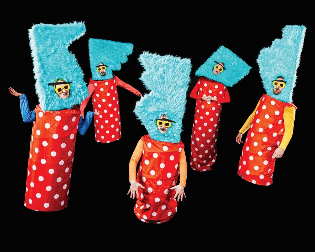 Five people wear polka dot tubes with large fuzzy blue headresses and sunglasses.