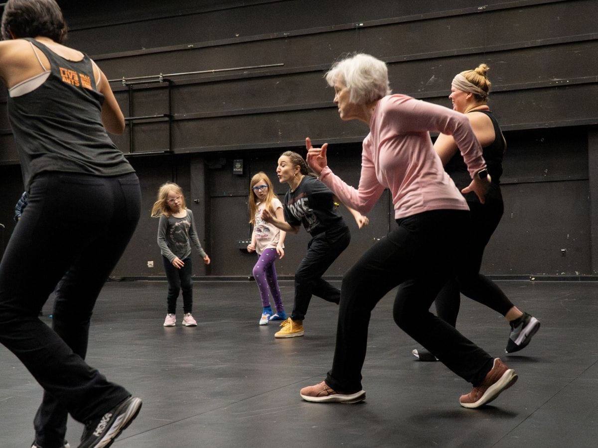 Two children and four older women are in a black box studio dancing.