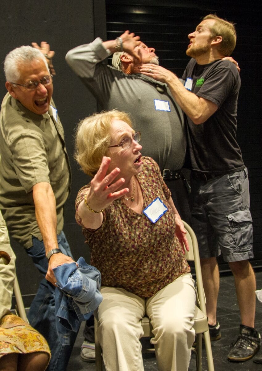 An older woman sits while others surround her doing a memory improvement activity.