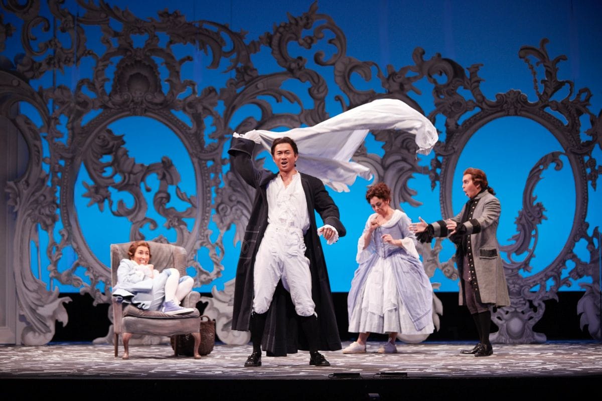 A man waves a bedshirt above his head while three people exclaim behind him.