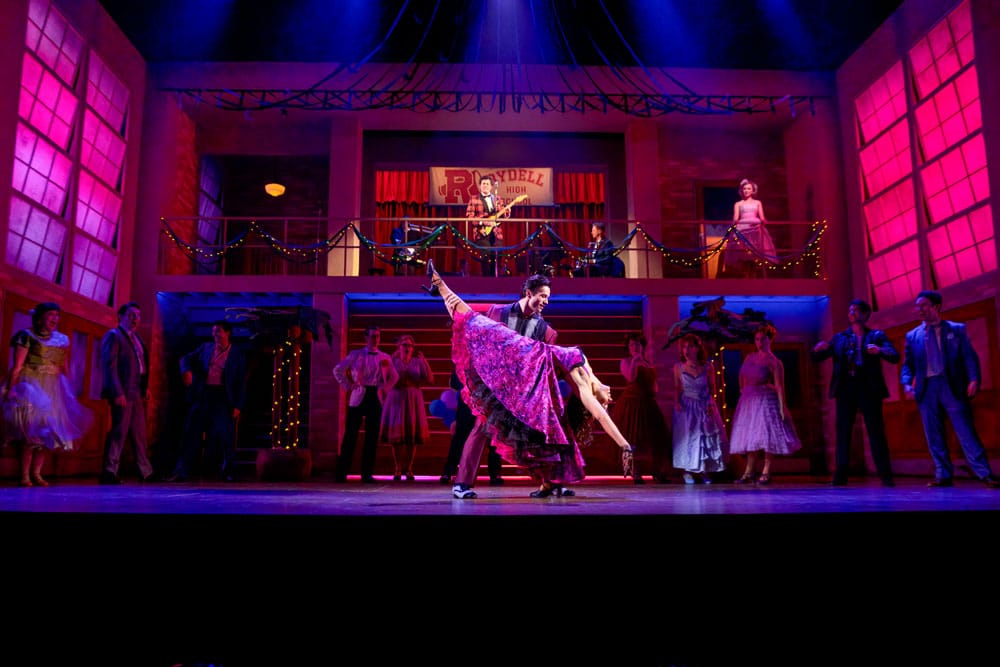 On a dance floor, people stand around watching a man who is dipping a woman with her leg high in the air.