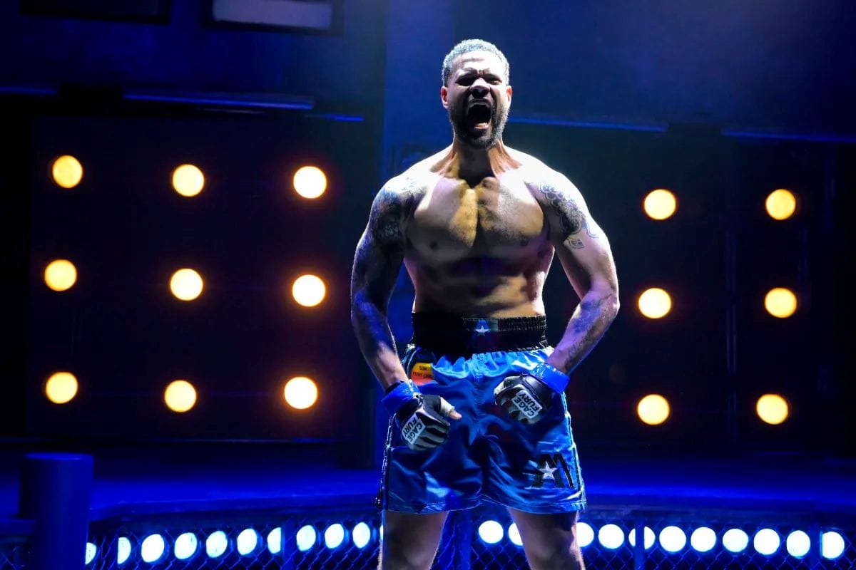 A boxer stands in a ring ready for a fight as he flexes and yells.