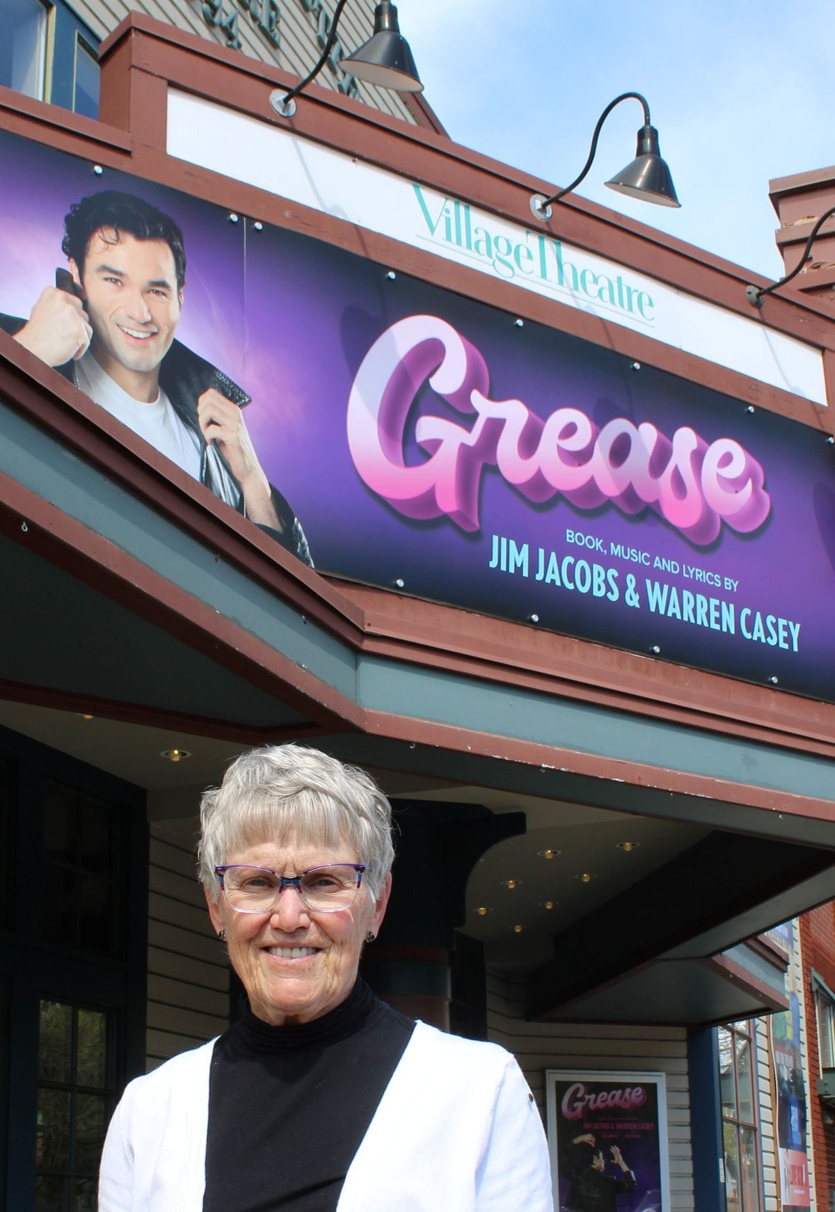 Marilyn Morrow stands outside of Village Theatre with the marquee for "Grease" in the background.