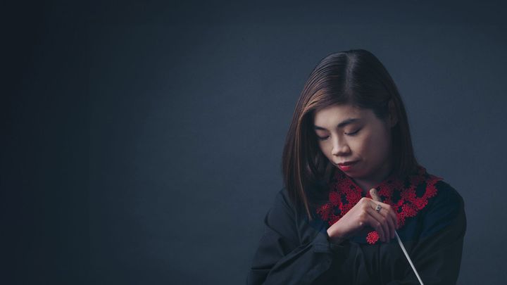 A press photo of Elim Chan. She holds a conductor's baton with her head down.