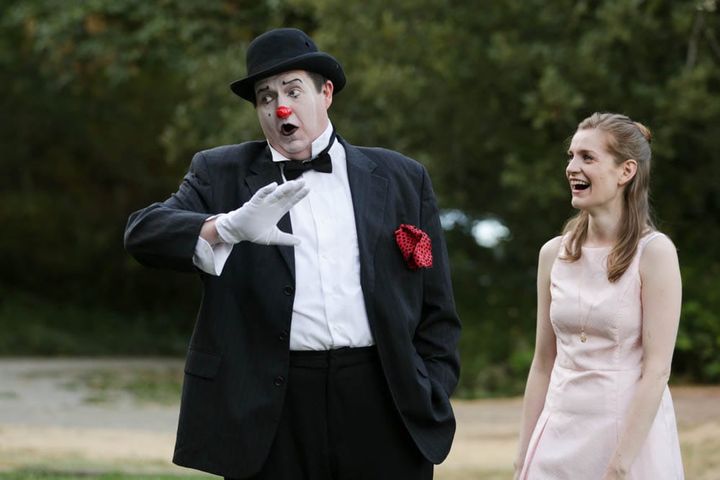 A man with clown makeup wears a tux while a women looks on laughing.