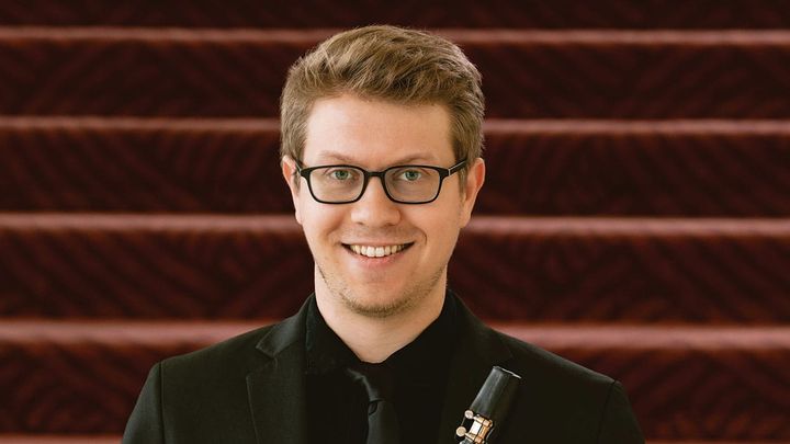 A press shot of Matthew Griffith holding his clarinet in front of stairs.