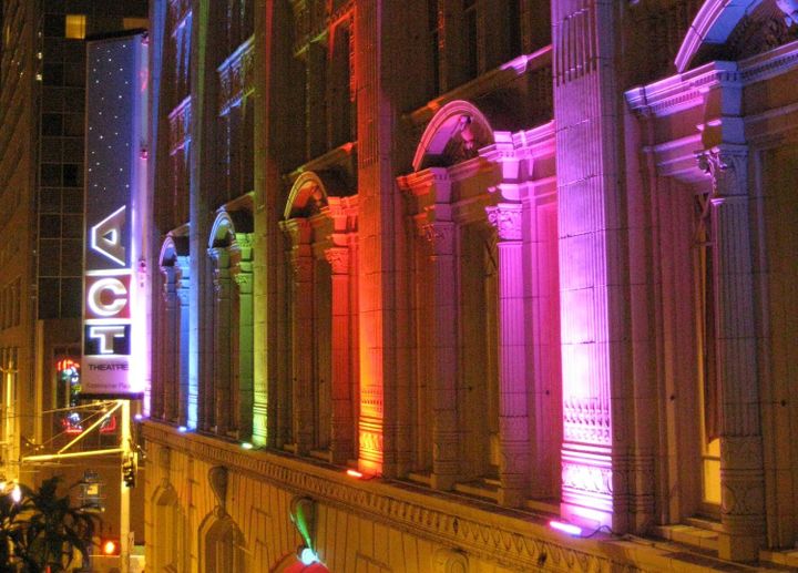 The outside of ACT Theatre at night with the building lit up with rainbow lights.