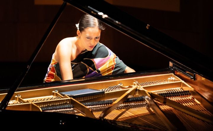 Pianist Mahani Teave plays the piano, concentration on the keys, with the piano open in the forefront.