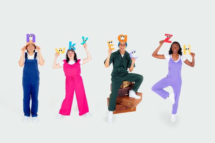 Four people stand in front of a white backdrop smiling and holding cutouts of letters above their heads.