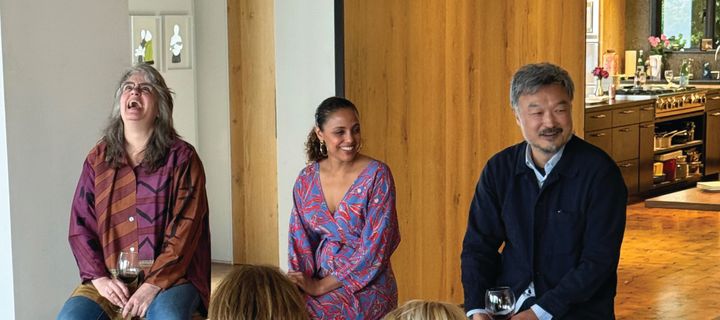 Three people sit together in front of a crowd laughing and smiling.