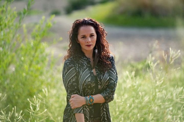 Larissa FastHorse stands in a field with large plants surrounding her.