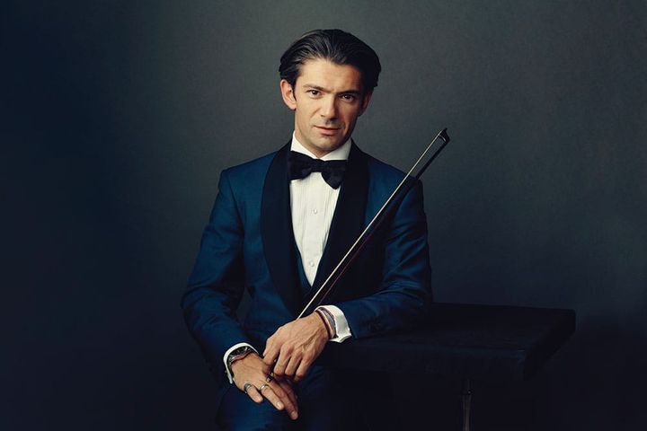 Cellist Gautier Capuçon wears a blue tux and holds his instrument, looking at the camera.