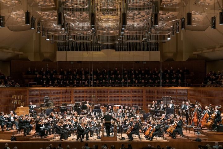 A symphony plays on stage with a large chorus in the back.