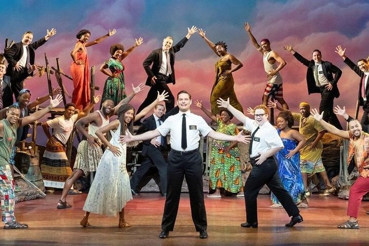 A large group of actors on stage all have their hands stretched towards a mormon missionary in the middle with his arms outstretched.