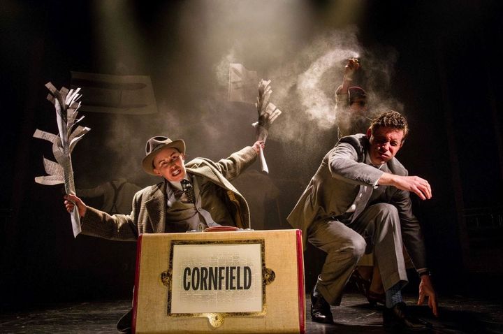 Two men in suits are burning paper on their knees behind a suitcase.