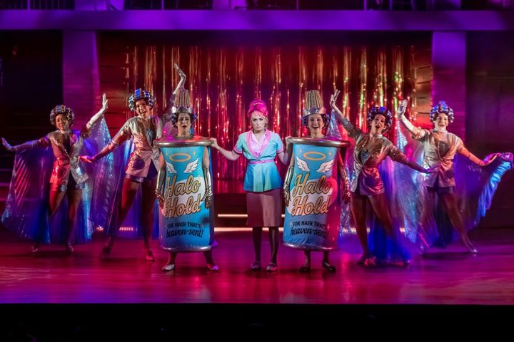 Two women are dressed as hairspray cans and others are dancing in salon garb.