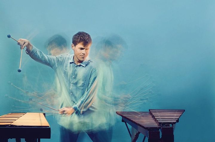 A blended image of a man playing two different versions of xylophones that are on either side of him.