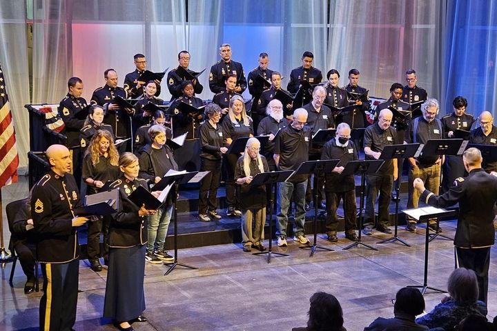 A group of veterans and current military memebers in uniform stand on risers and sing in front of an audience.