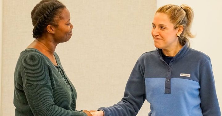 Two women smile and shake hands.