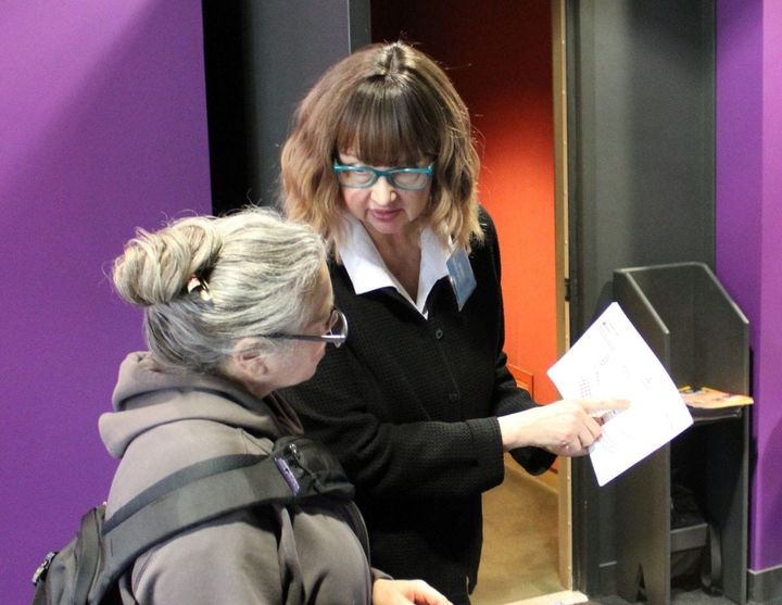 Two women talk, one is helping the other in a theatre lobby.