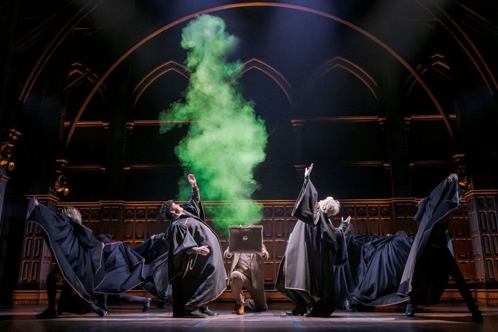 Boys wearing Hogwarts robes stand back from a cauldron as it explodes with green smoke.