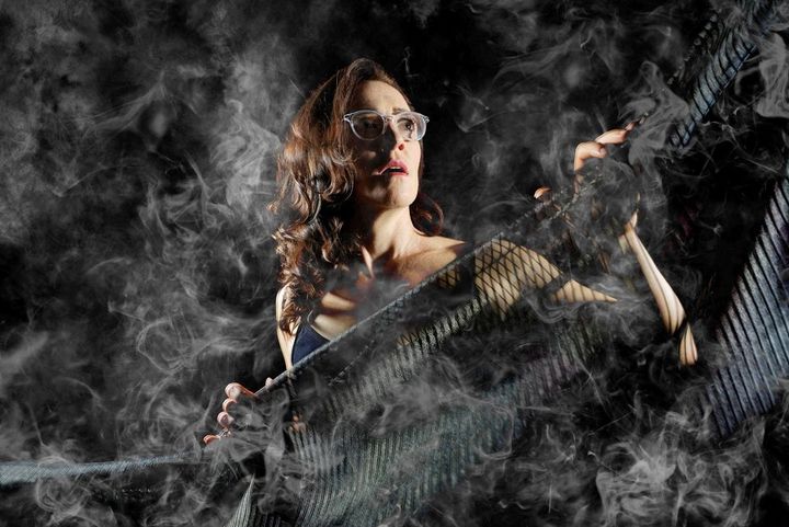 A woman looks frightened against a black background and surrounded by smoke.