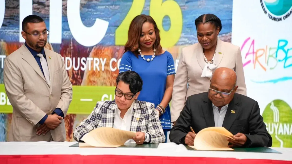 Susan Rodrigues and Edmund Bartlett sit at a table signing documents during SOTIC 2026, while three officials stand behind them.