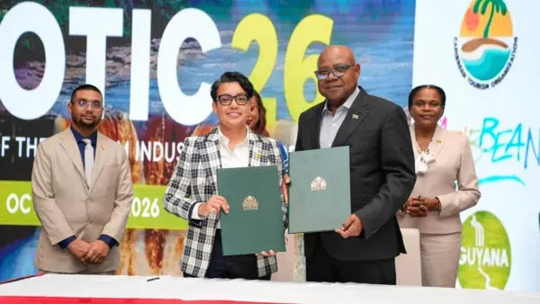 Susan Rodrigues and Edmund Bartlett hold up the signed Guyana–Jamaica tourism cooperation agreement at SOTIC 2026, with three officials standing behind them.