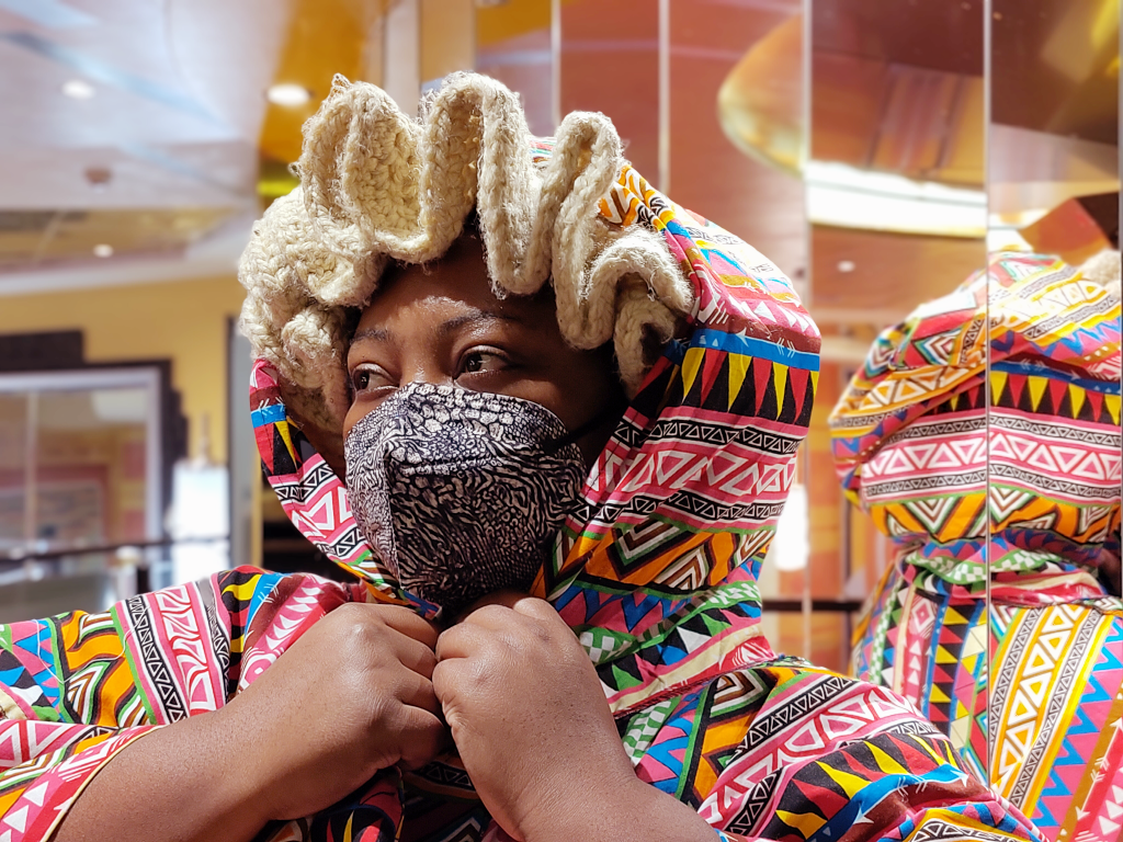 A black person in colorful african clothes looking away while wearing a pattened n95 mask. 