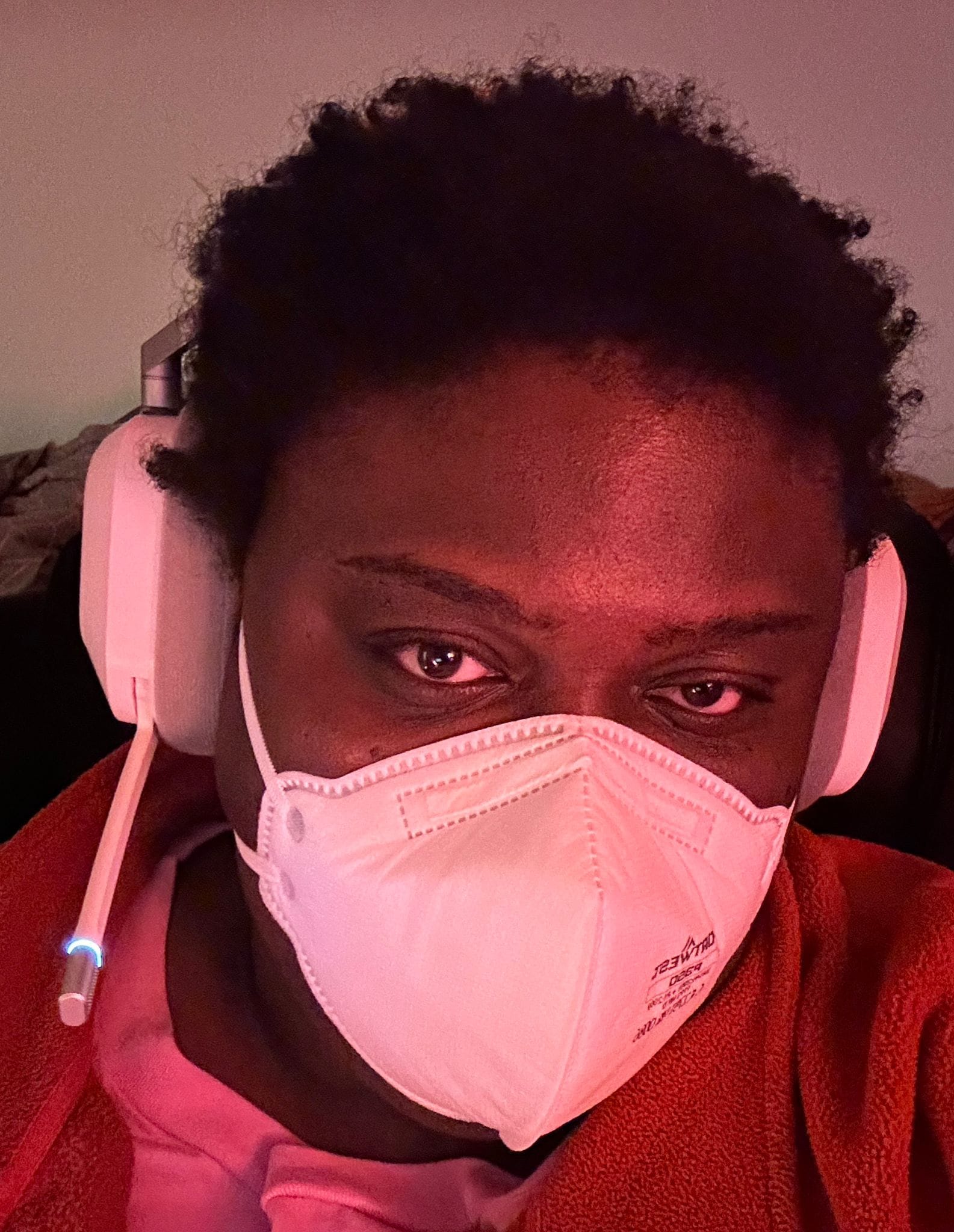 A black person looking into the camera wearing a white n95 mask and white headphones. 