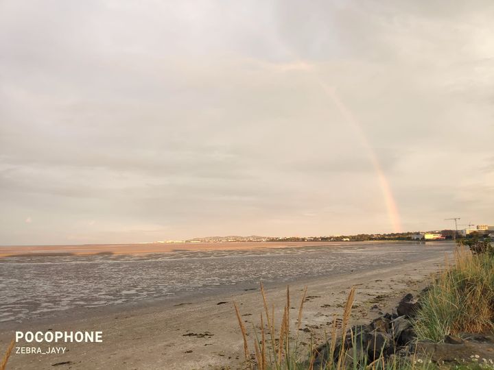A picture of a shore there's a faint rainbow in the back