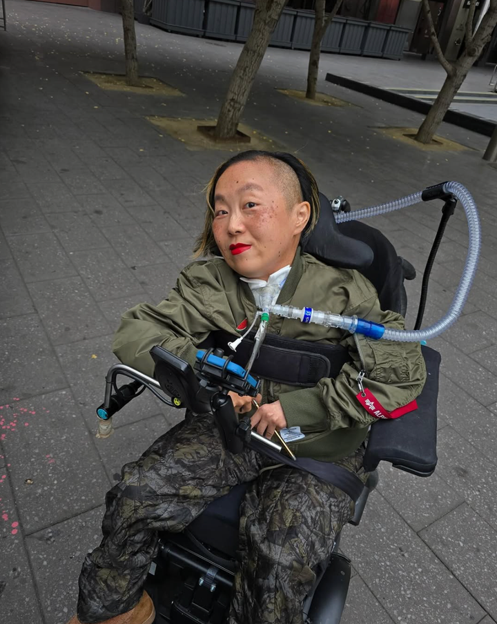 Asian American woman in a wheelchair with a tracheotomy at her neck connected to a ventilator.