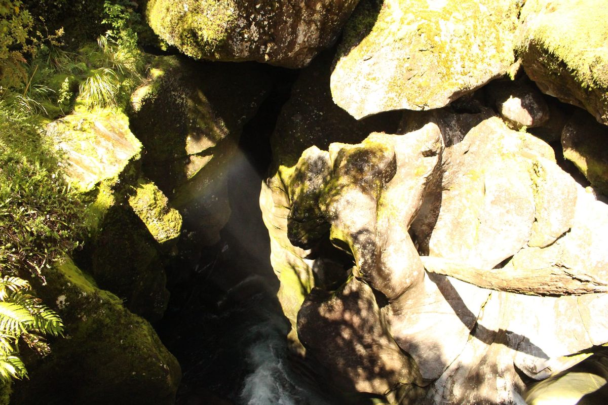 A river flowing into a cavern with light being reflected to reveal a rainbow.