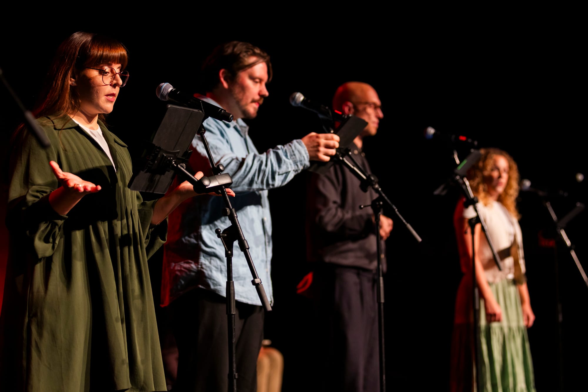 The live recording of Sherlock & Co. at The Rest Is Fest, with four voice actors standing on stage performing with microphones.
