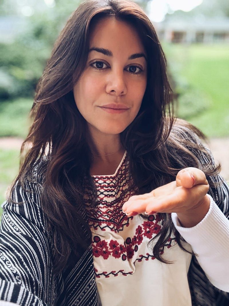The image shows a woman with long, dark hair, wearing a white top with red embroidery and a black-and-white shawl draped over