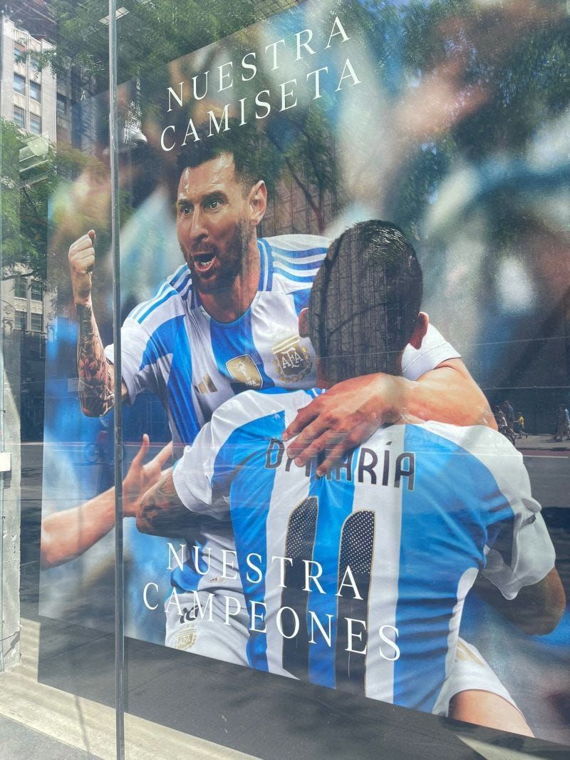 Poster of Messi giving teammate celebratory hug on soccer field, text on the advertisement reads “Nuestras Camisetas Nuestras