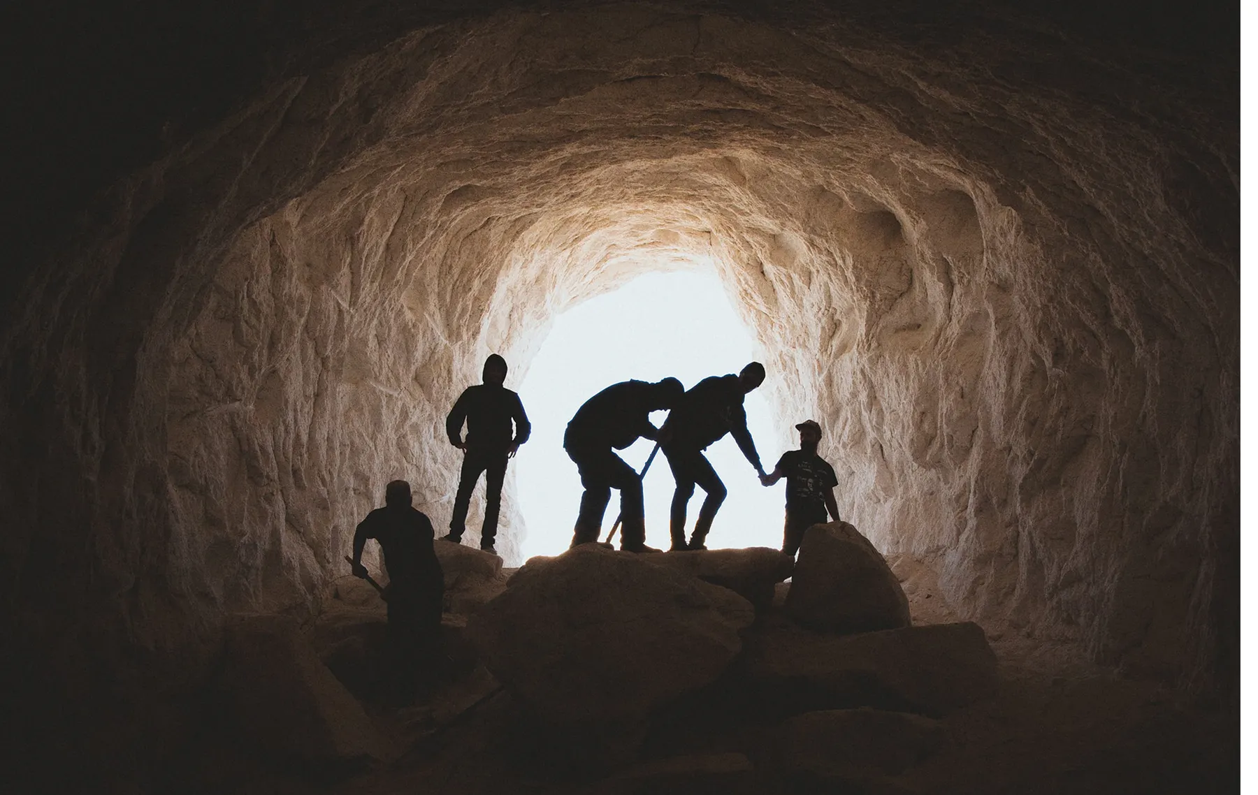 Silhouette of miners in at mouth of tunnel.