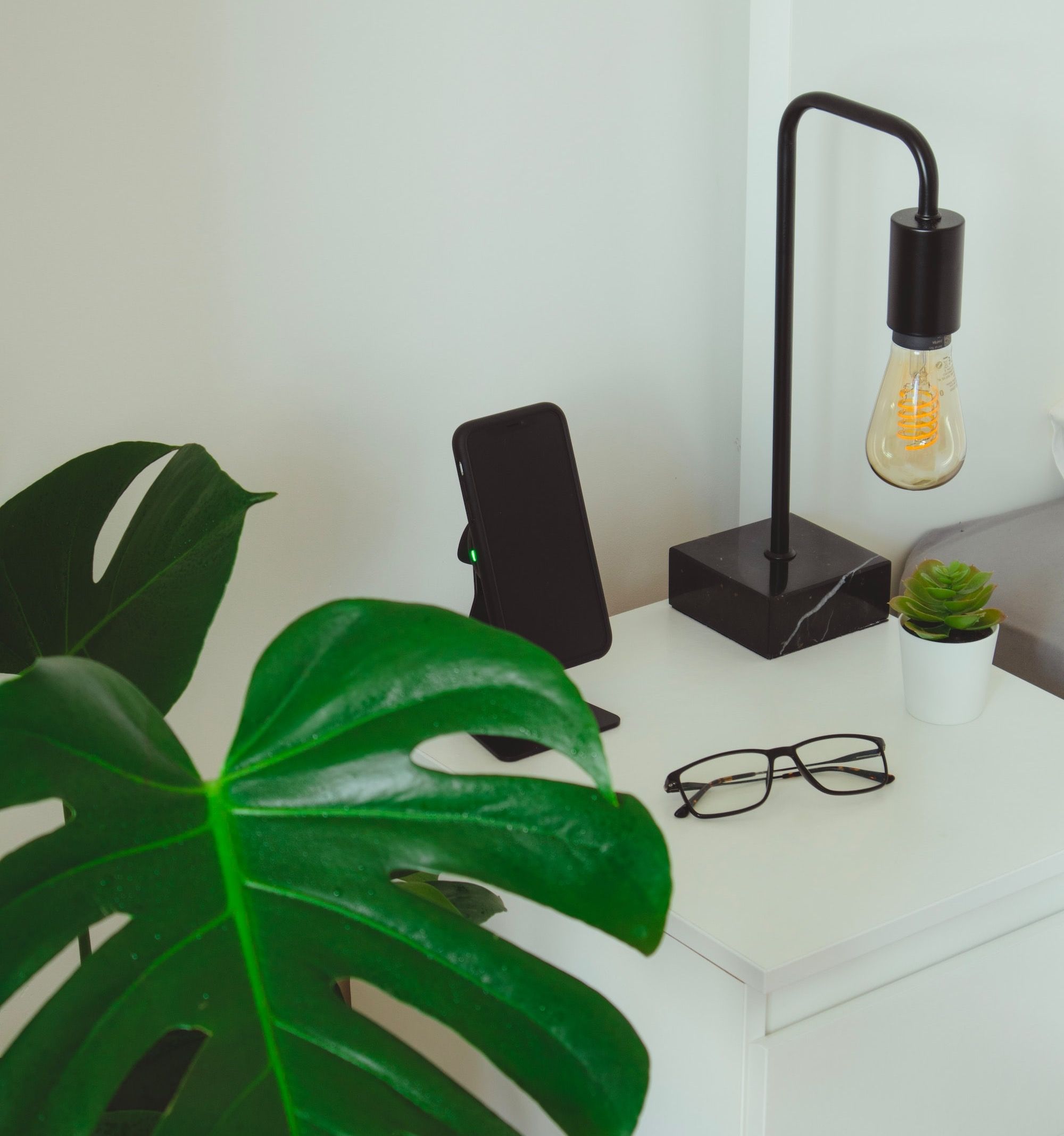 black framed eyeglasses beside black smartphone and green plant
