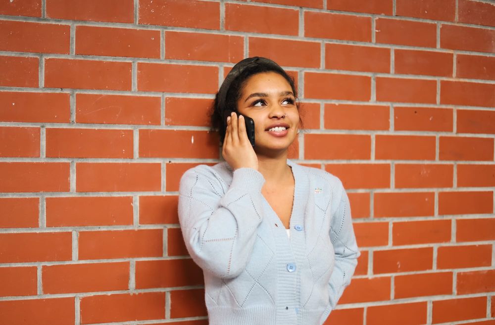 Woman talking on phone by brick wall post image