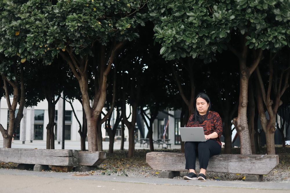Focused woman working on laptop outdoors under trees post image
