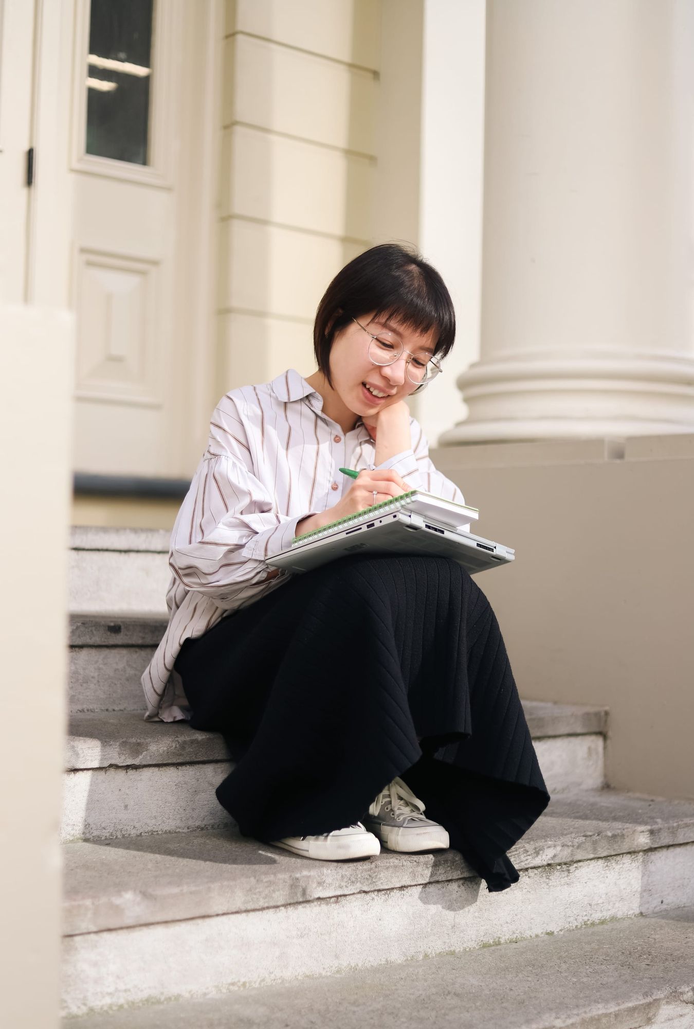 Woman writing notes on steps with laptop