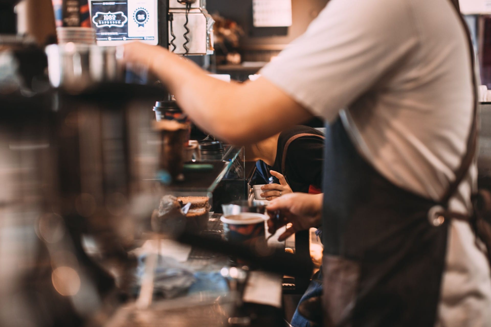 A barista working the coffee machine behind a busy cafe counter
