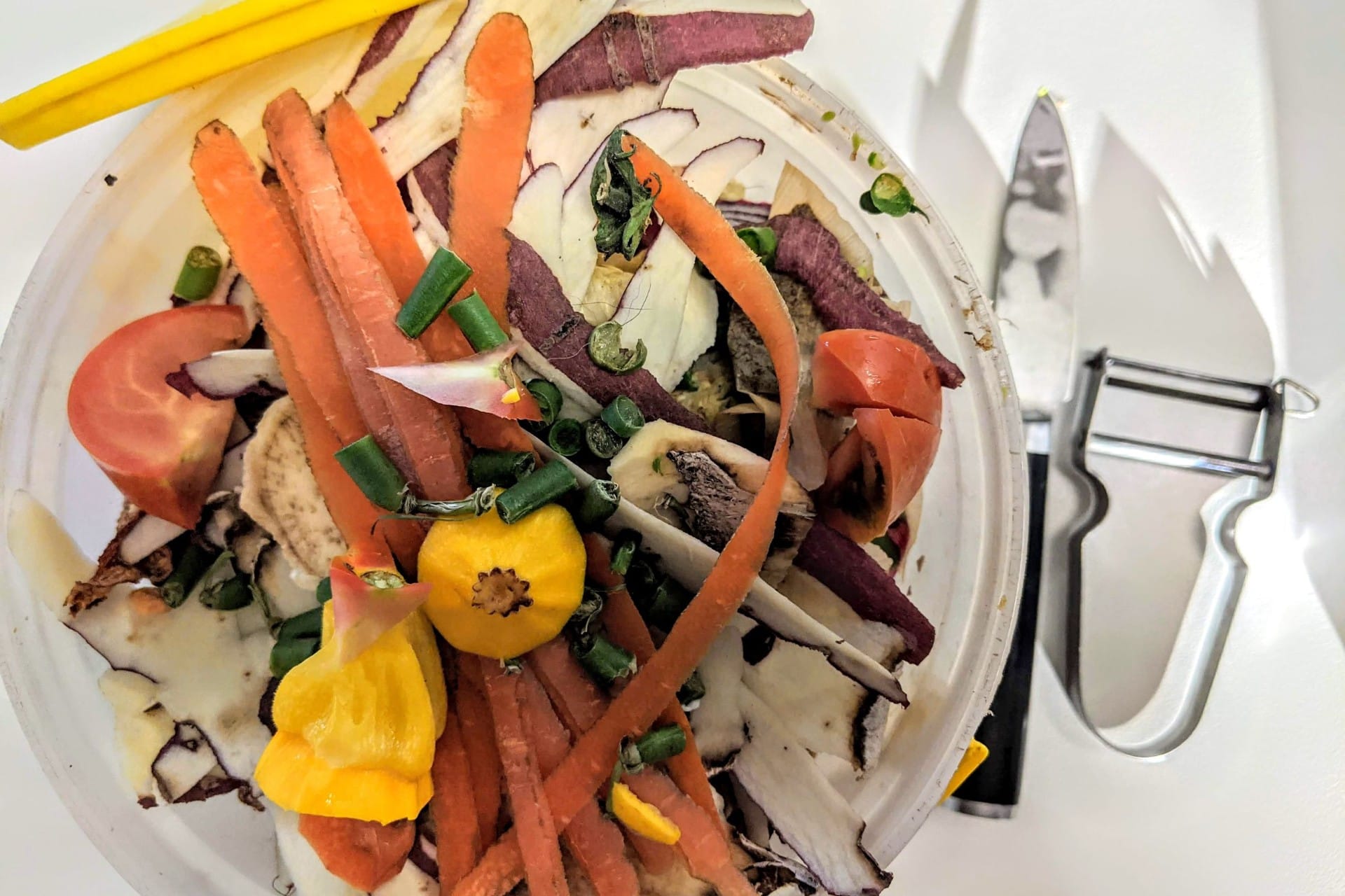 A plate of vegetable peelings and trimmings beside a peeler and a knife