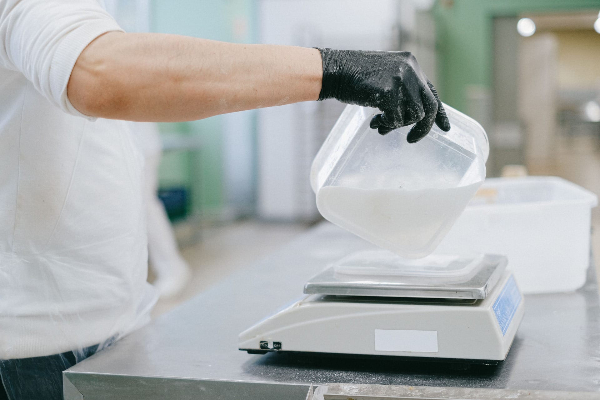 A chef weighing an ingredient into a container on a platform scale, portioning to control gross profit