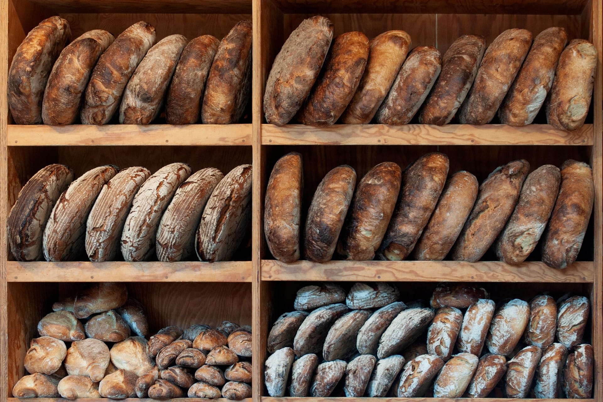 Racks of artisan sourdough loaves stacked on wooden shelves in a bakery
