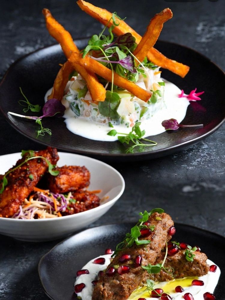 Small plates on a dark plate, crispy chicken bites with slaw and carrot sticks, finished with herbs and flowers.