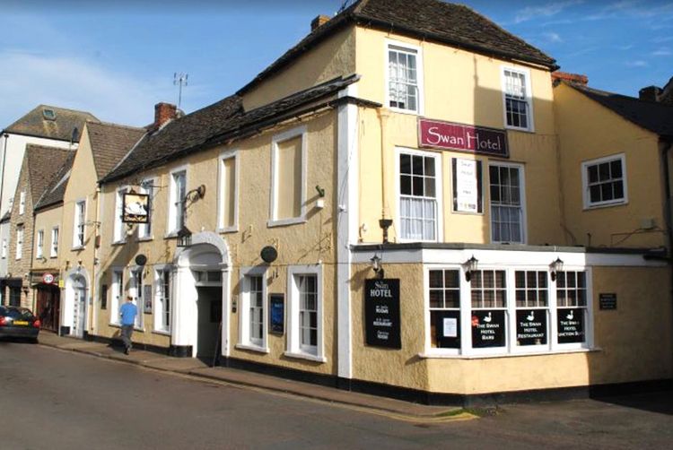 Street view of The Swan Hotel at Wotton-under-Edge, a cream and white painted building with a red hotel sign.