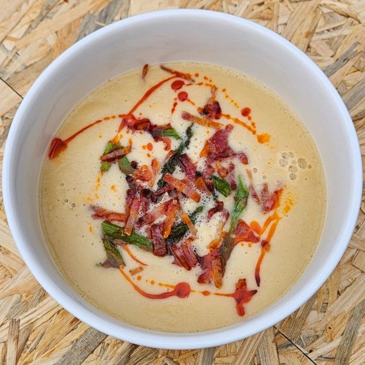 White bowl of creamy leek and butter bean soup topped with crispy chorizo, greens and chilli oil, seen from above.